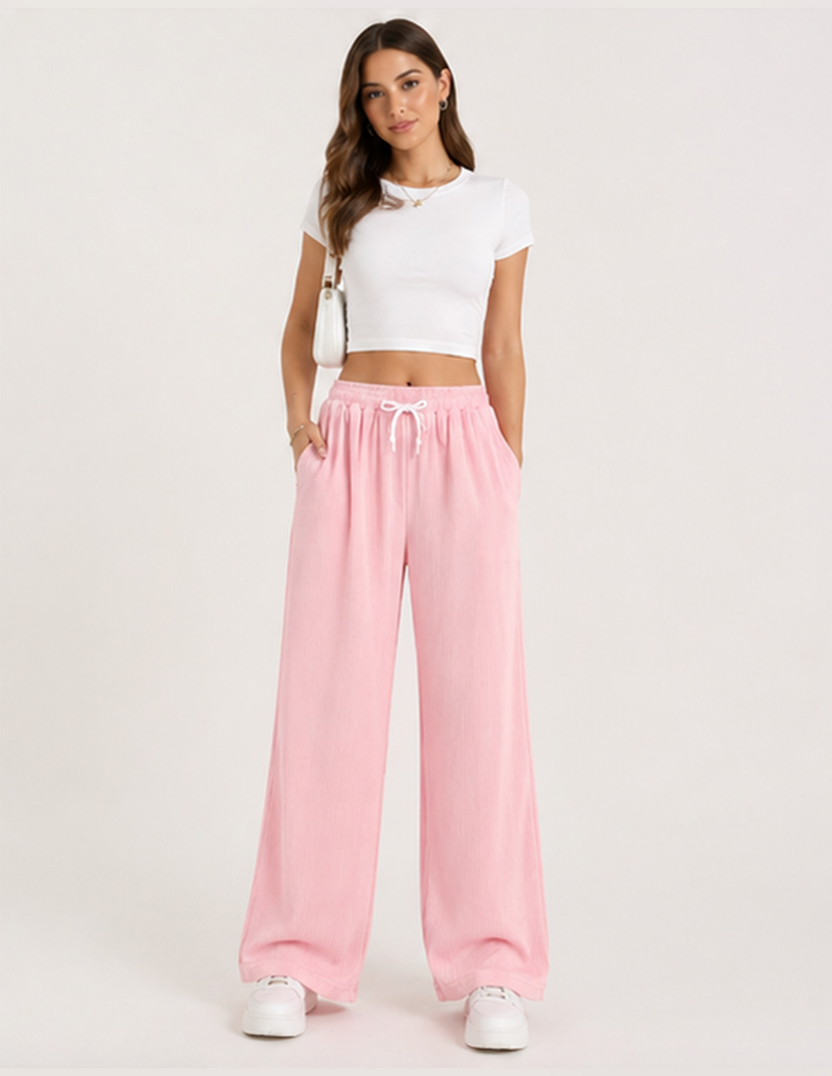 Woman wearing a white crop top and pink sweatpants on a white background