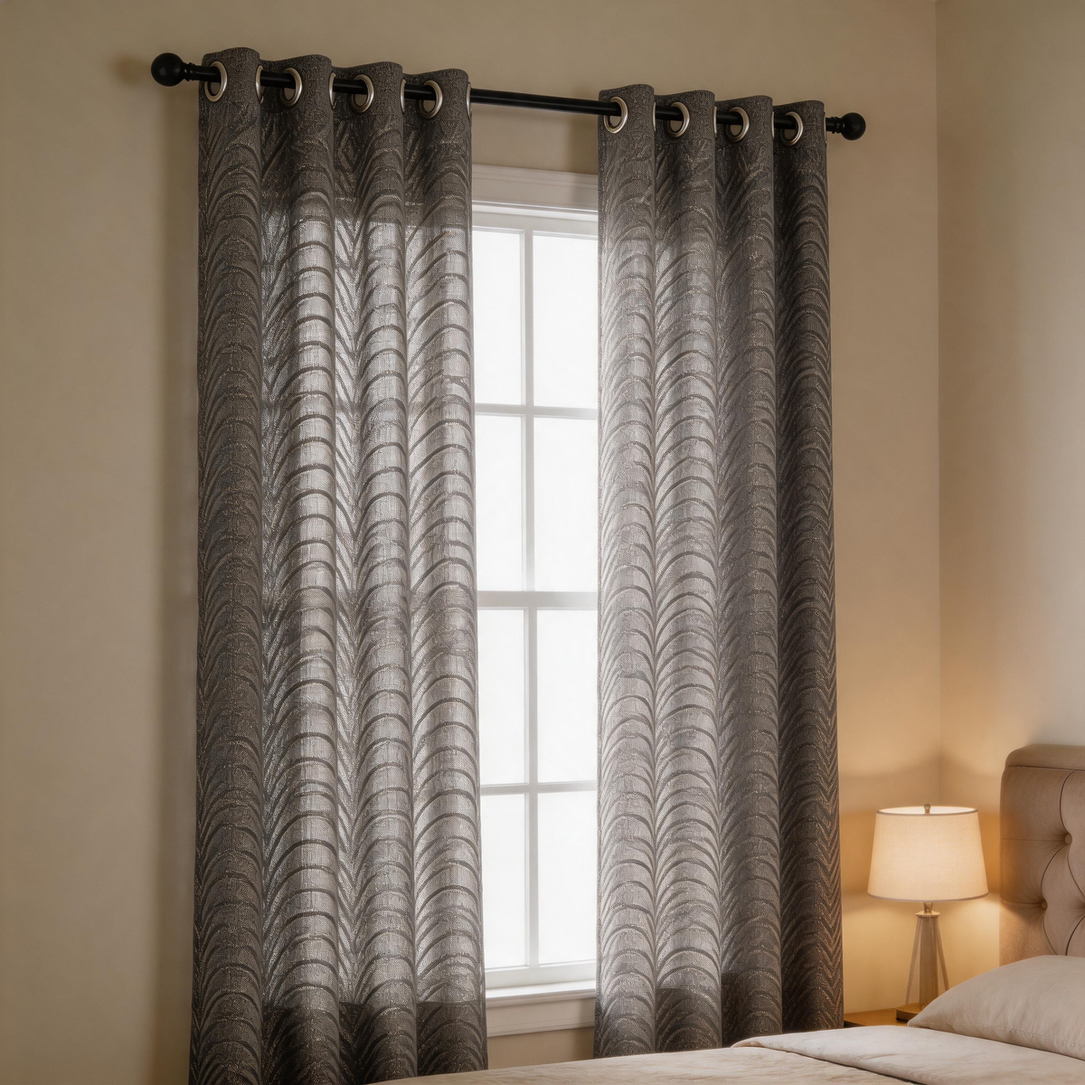 Pair of grey Antigua sheer chenille grommet curtains with a scalloped wave pattern hanging over a bedroom window