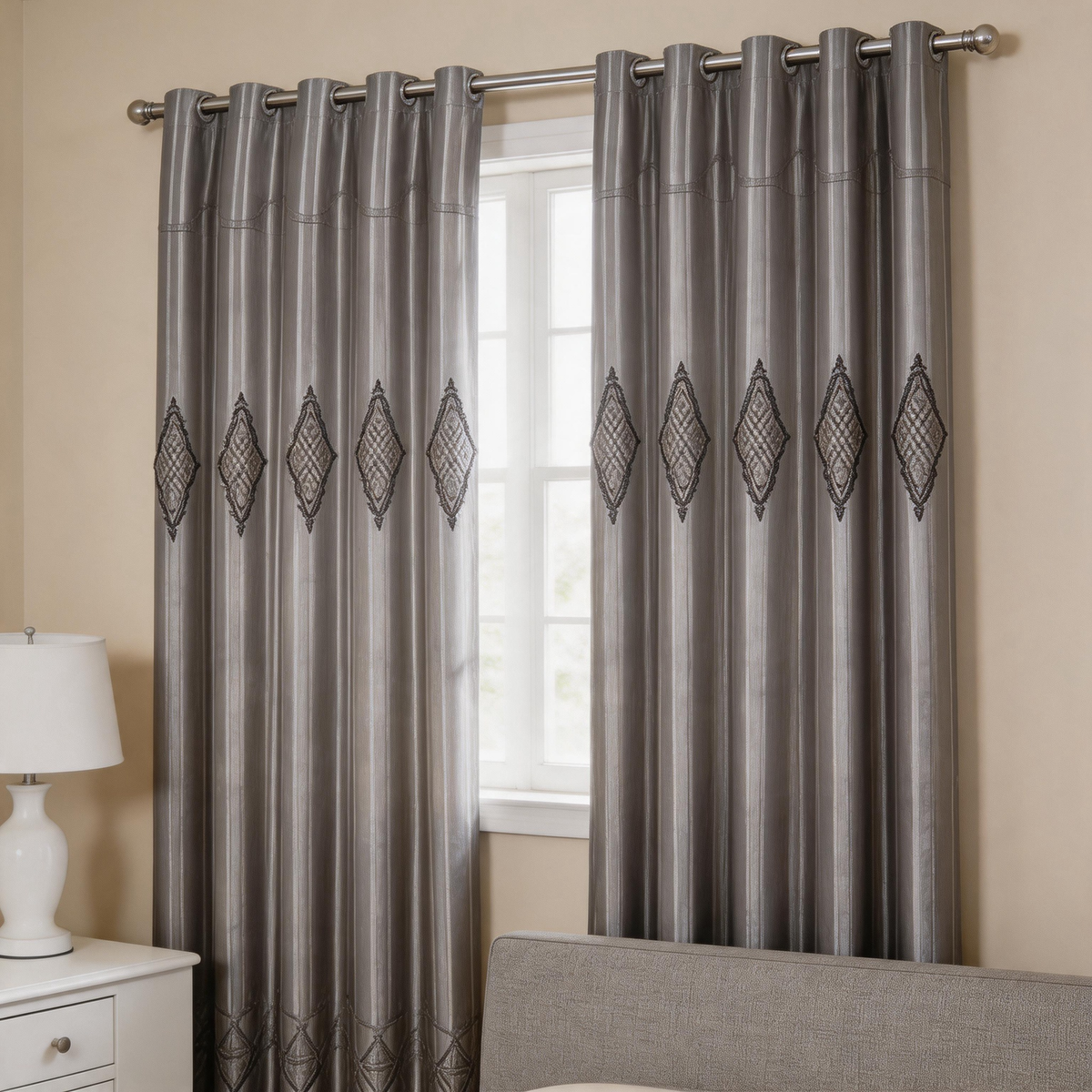 A pair of gray grommet curtains with a subtle vertical sheen and a repeating black diamond pattern, hanging on a silver rod over a window in a bedroom setting.