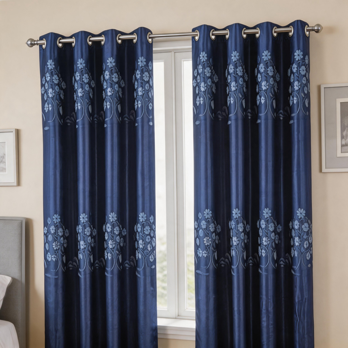 A pair of navy blue grommet curtains with a light blue floral damask pattern, hanging on a silver metal rod in a bedroom setting.