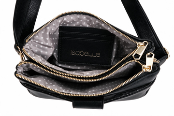Black faux-leather crossbody bag shown open, featuring a gray and white polka dot interior lining with a black card holder displaying the brand name 'Isabelle' in gold lettering, and gold-tone zippers.