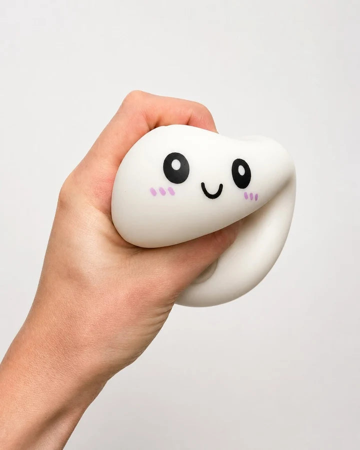 A hand holding a white, squishy, tooth-shaped stress toy with a cute black face and pink cheeks against a plain light gray background.