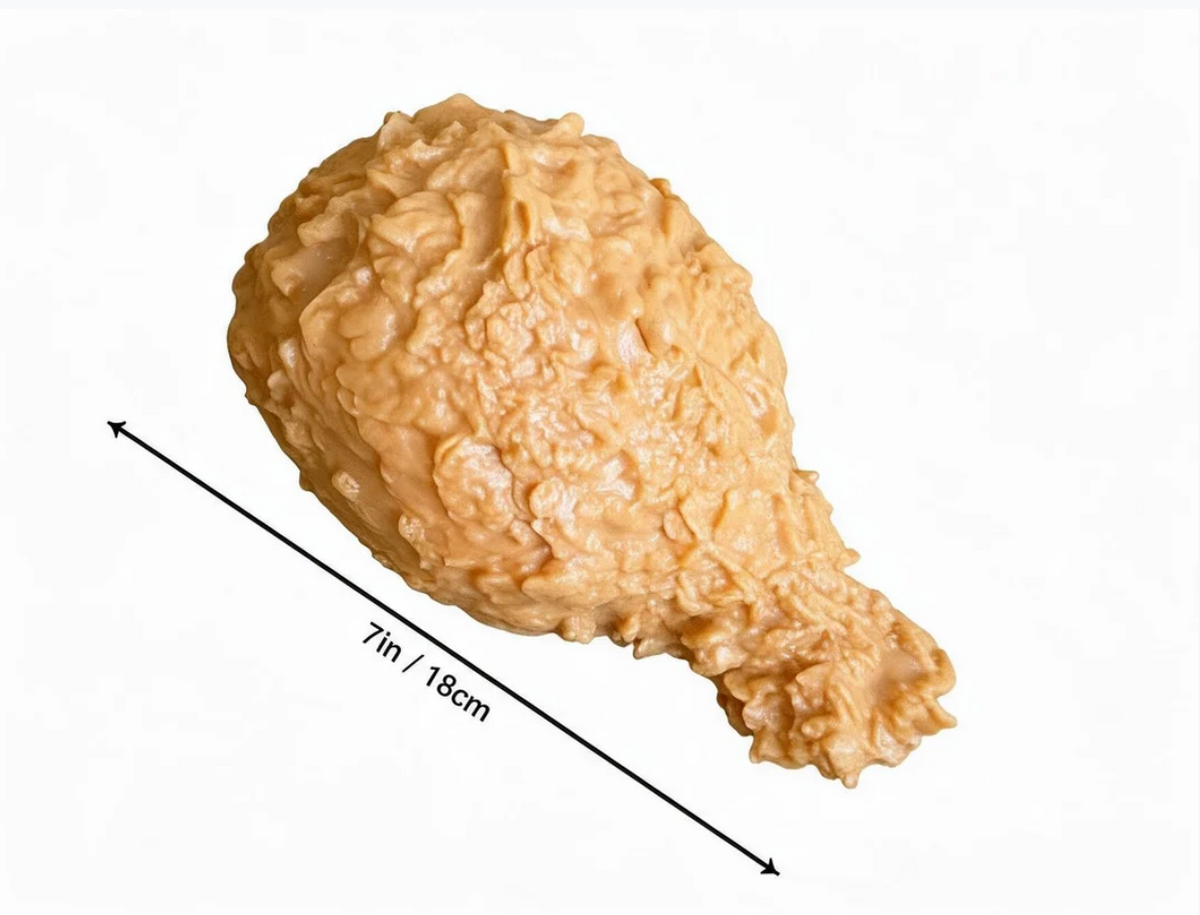 A realistic fried chicken drumstick prop or toy shown on a white background with a black measurement arrow and text indicating 7 in / 18 cm length.